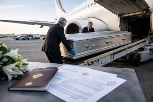 Deux agents funéraires chargent un cercueil hermétique dans la soute d’un avion pour un rapatriement international, avec documents officiels et passeport au premier plan.